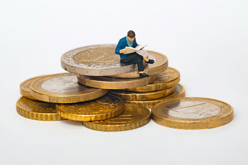 Man sitting on pile of coins weighing the pros and cons of traditional vs. self-publishing